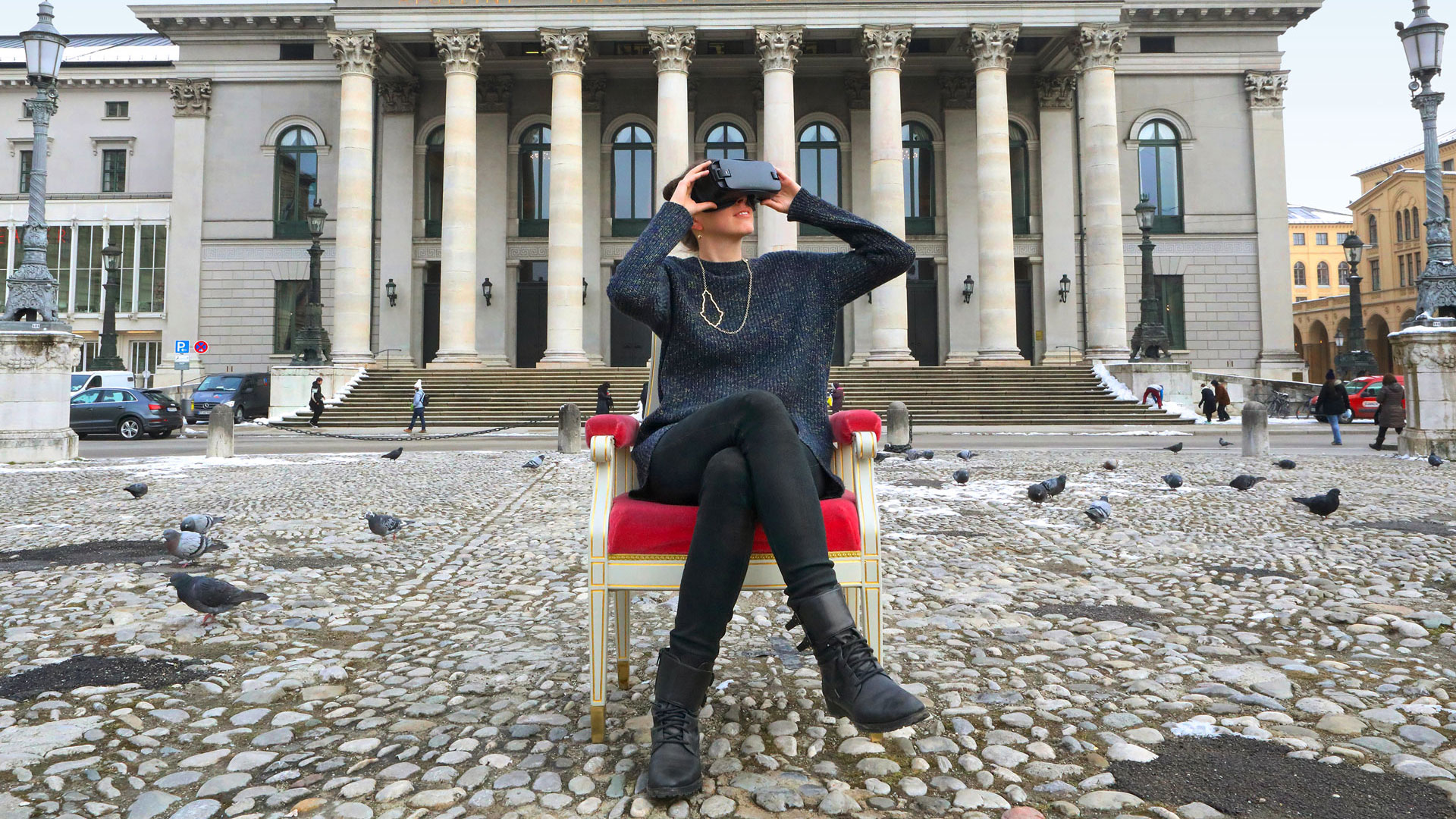 Frau sitzt mit Virtual-Reality-Brille vor der Bayerischen Staatsoper